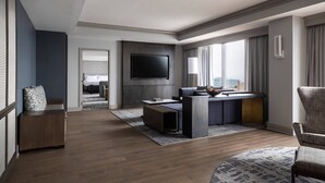 Une chambre d’hôtel moderne dotée d’un téléviseur à écran plat fixé au mur, d’un bureau avec une chaise, d’un canapé et d’une grande fenêtre avec des rideaux.