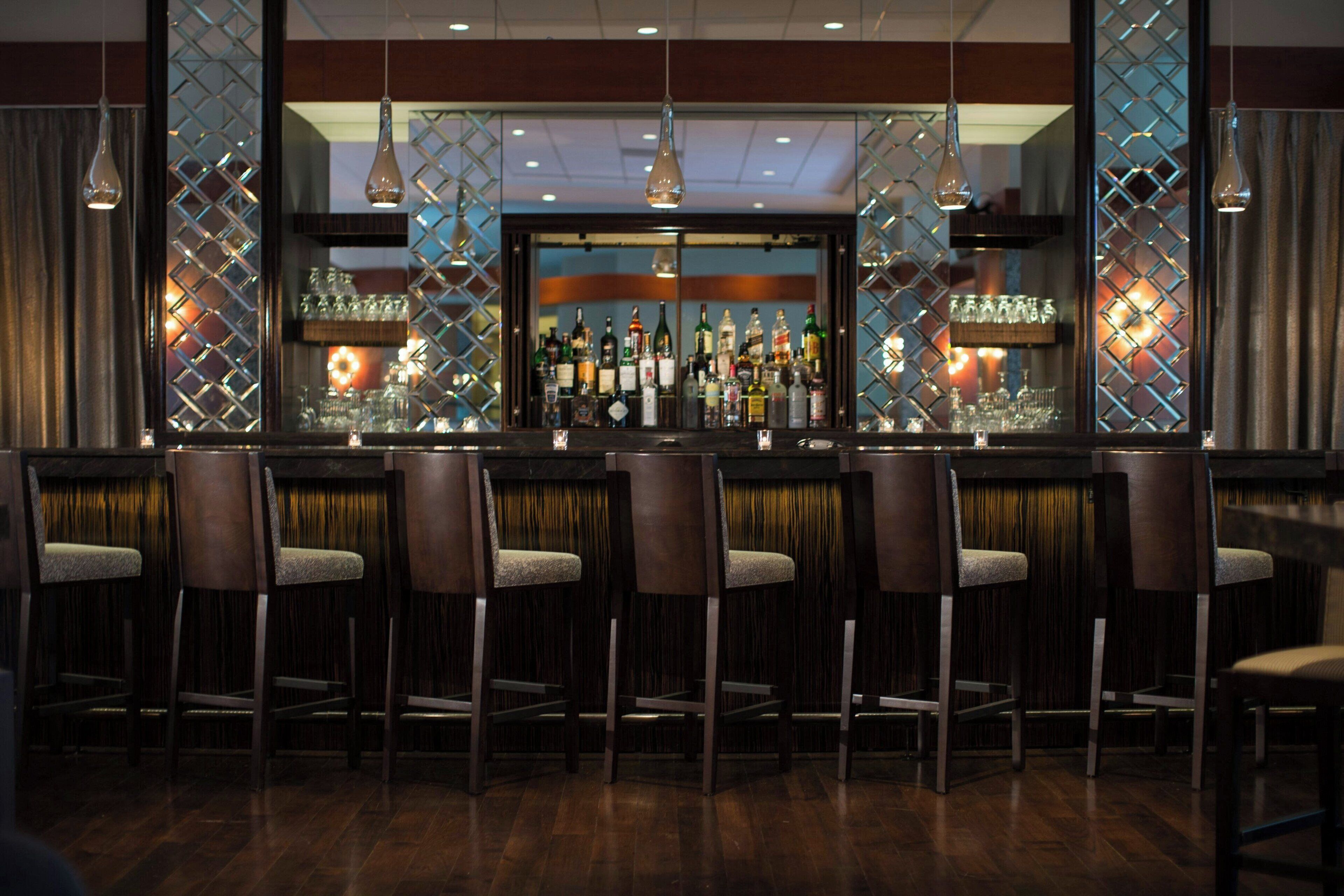 Zona de bar con varios taburetes, una barra y una variedad de botellas y vasos.