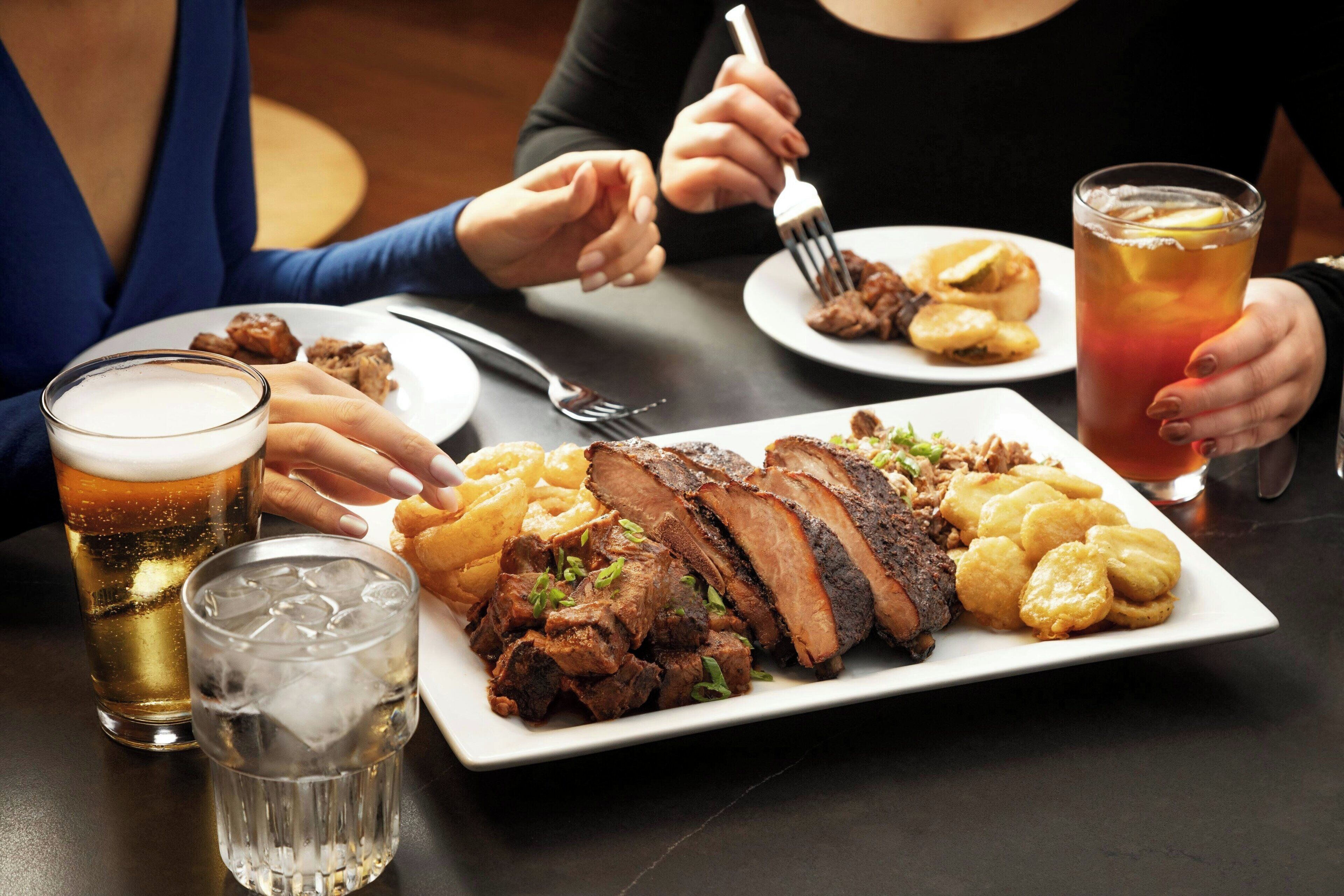 A dining table with a plate of food, two glasses of beer, and a glass of iced tea.
