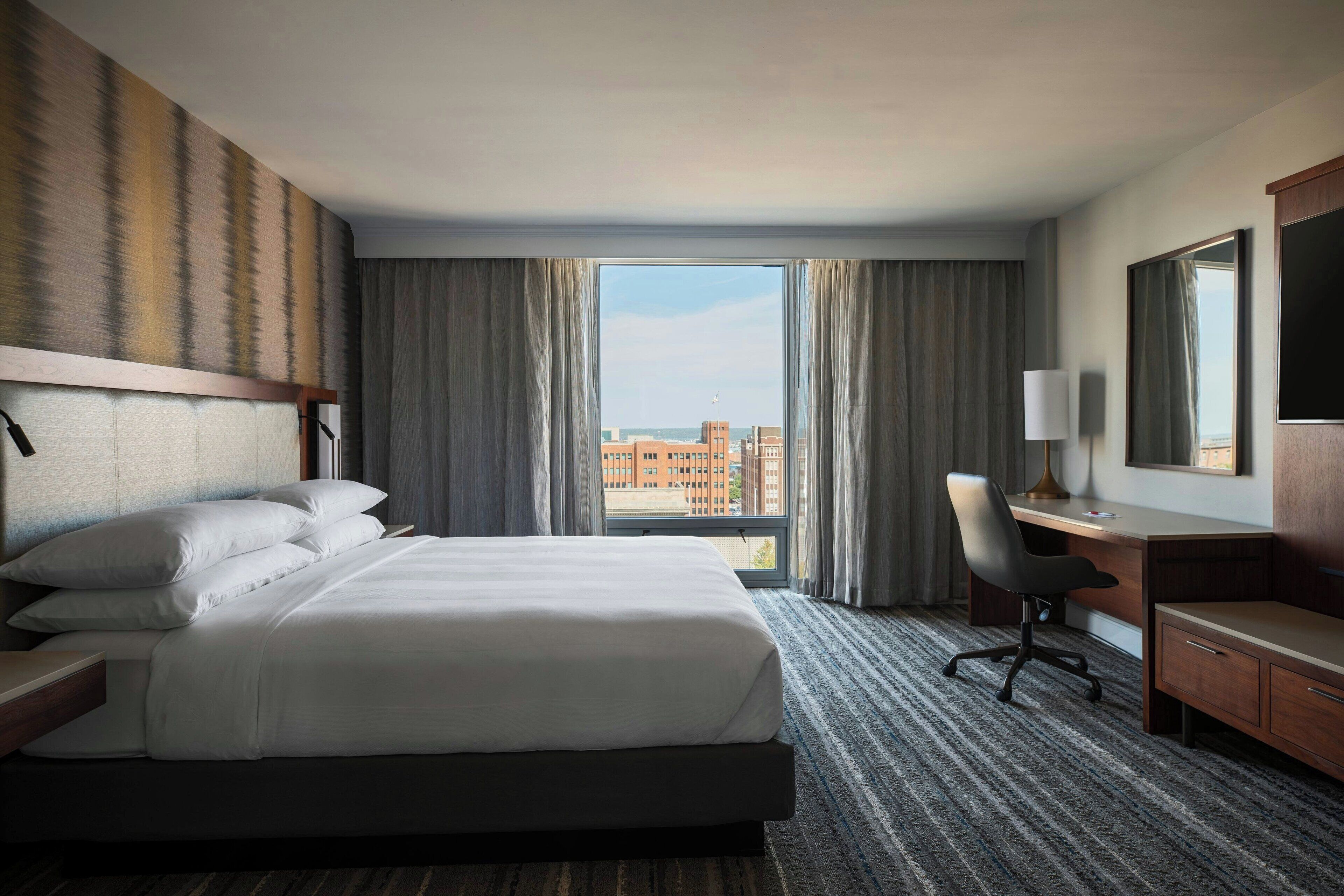 Une chambre d’hôtel avec un grand lit, un bureau, une chaise et un téléviseur.