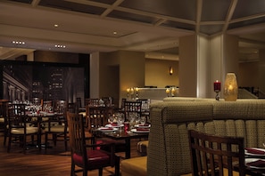 A restaurant with multiple dining tables and chairs, a patterned sofa, and candles on the tables.