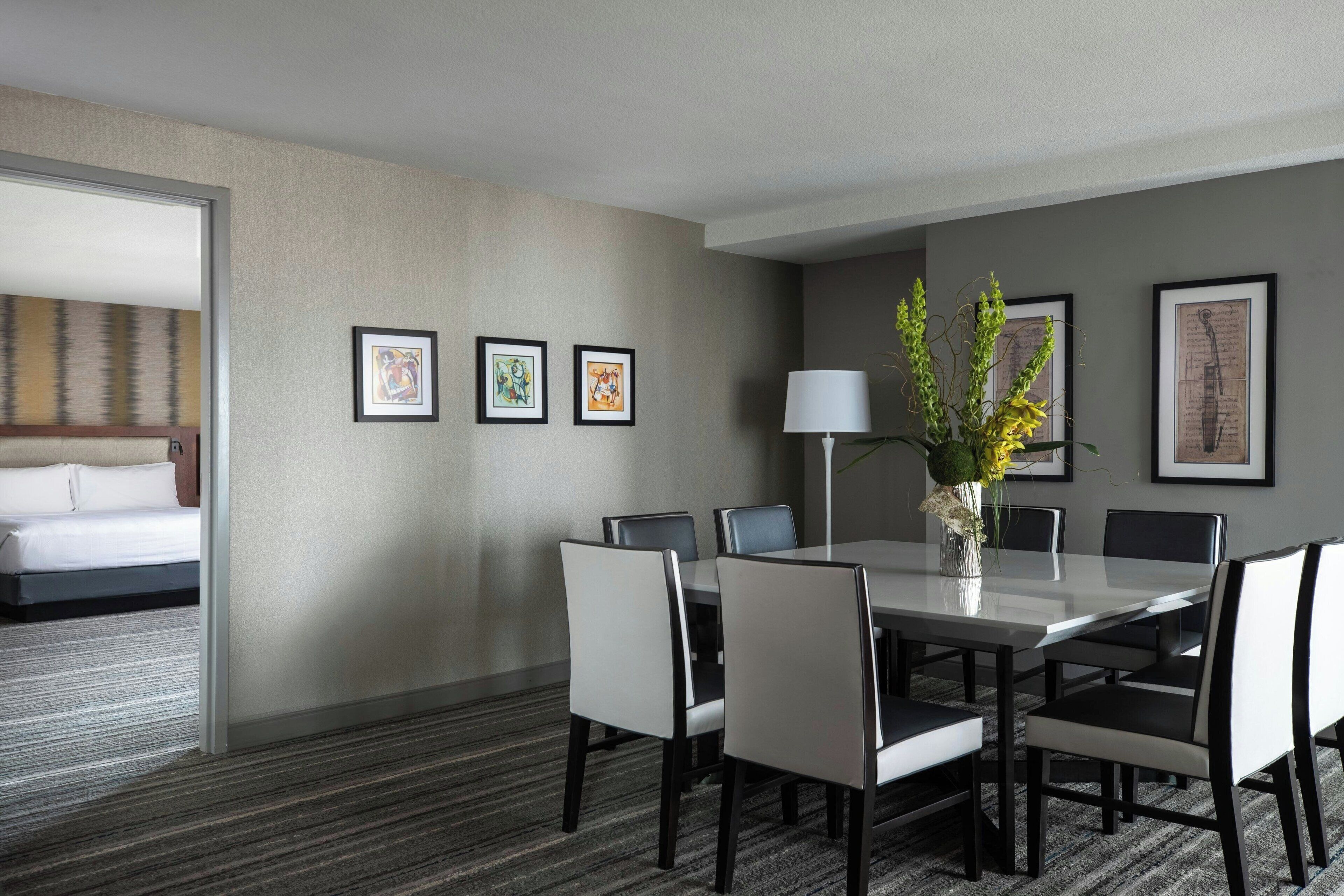 A hotel room with a dining area featuring a white table, black chairs, and framed artwork on the walls.