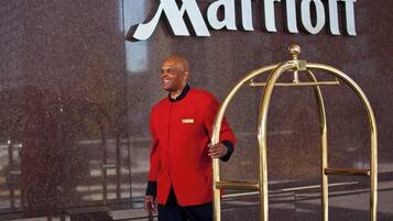Un hombre con uniforme rojo de pie frente a la entrada de un hotel Marriott, con puerta giratoria dorada.