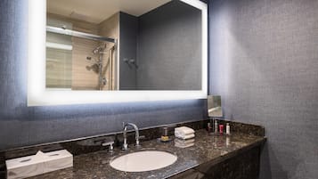 Un baño moderno con un espejo grande, encimera de granito y zona de ducha.