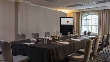 A conference room with a long table, chairs, a screen displaying the Marriott logo, and a window with curtains.