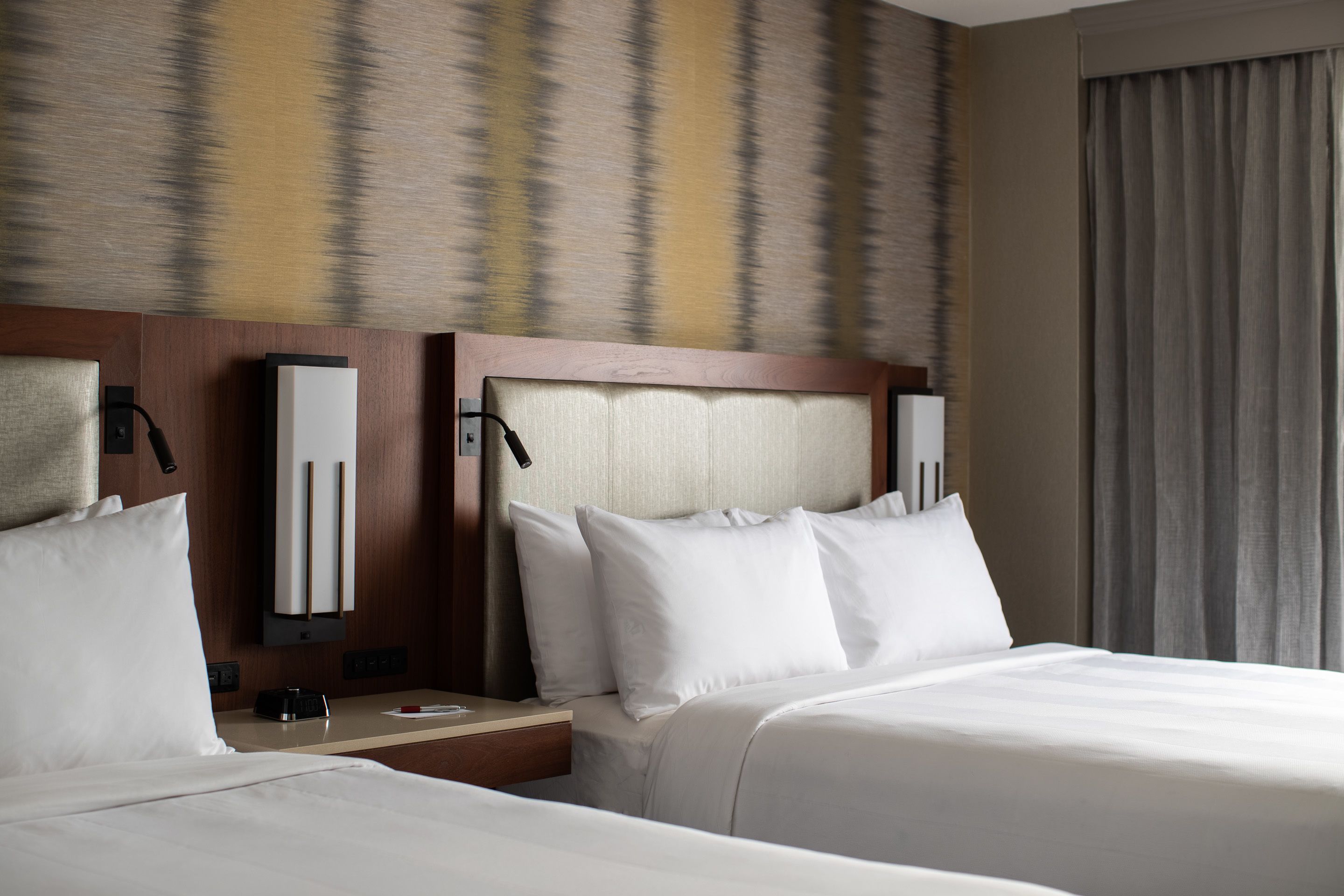 Une chambre d’hôtel avec deux lits, une table de chevet avec une lampe et un téléviseur fixé au mur.