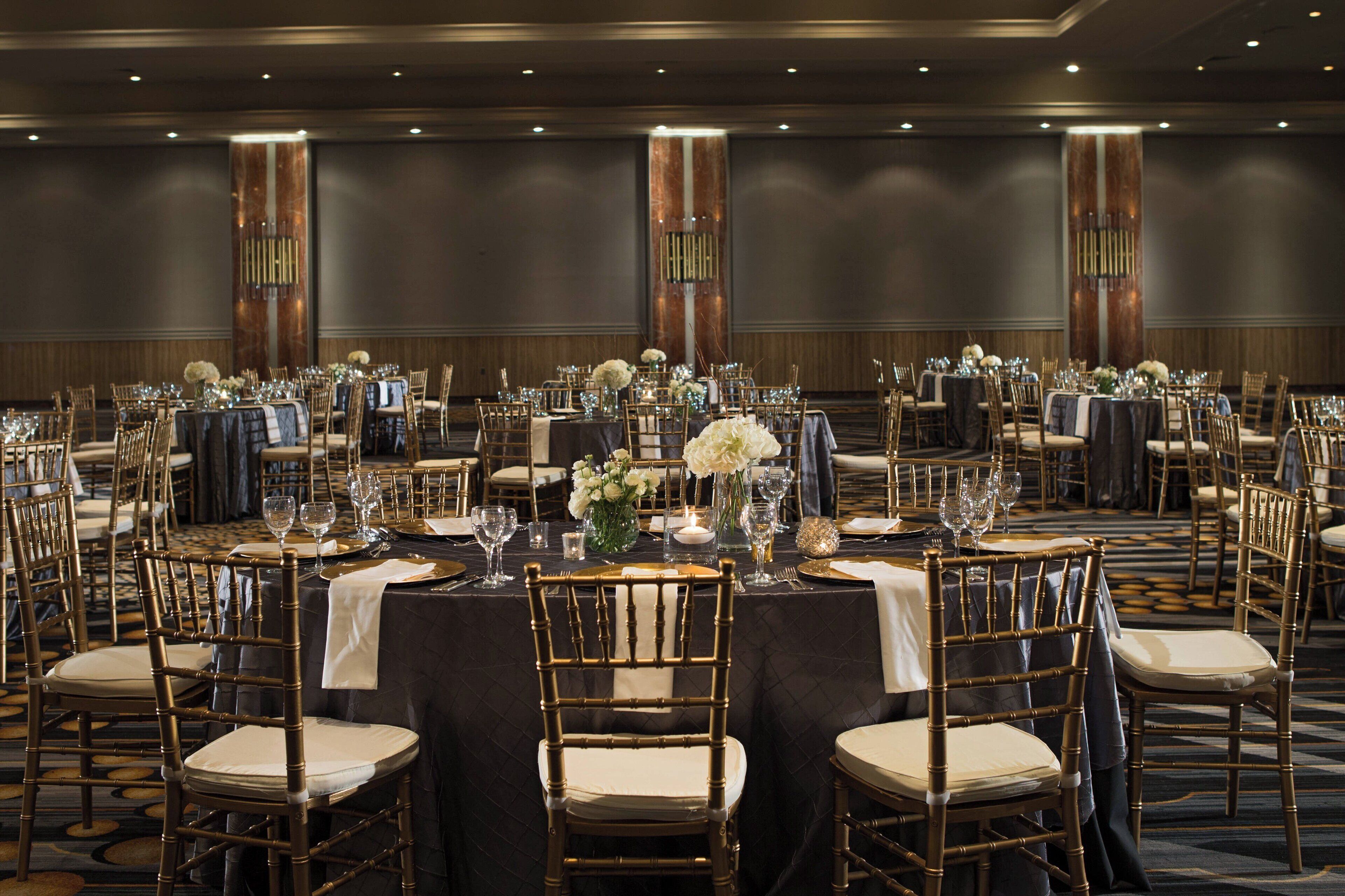 Un salón de banquetes con mesas redondas, sillas y centros de mesa florales.