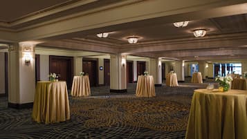 A spacious hotel lobby with multiple round tables, elegant chandeliers, and a patterned carpet.