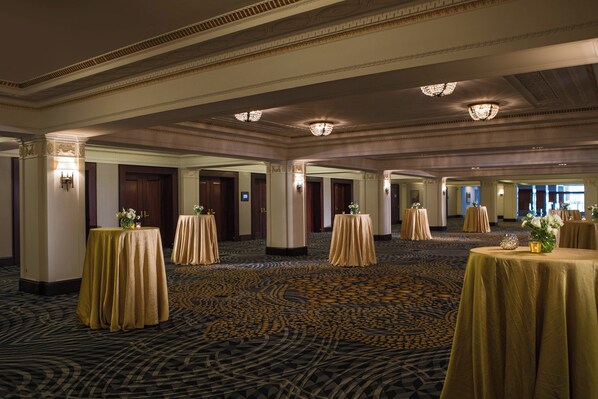 A spacious hotel lobby with multiple round tables, elegant chandeliers, and a patterned carpet.