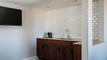 A modern kitchen with a white tiled backsplash, wooden cabinets, a stainless steel sink, and a flat-screen TV mounted on the wall.