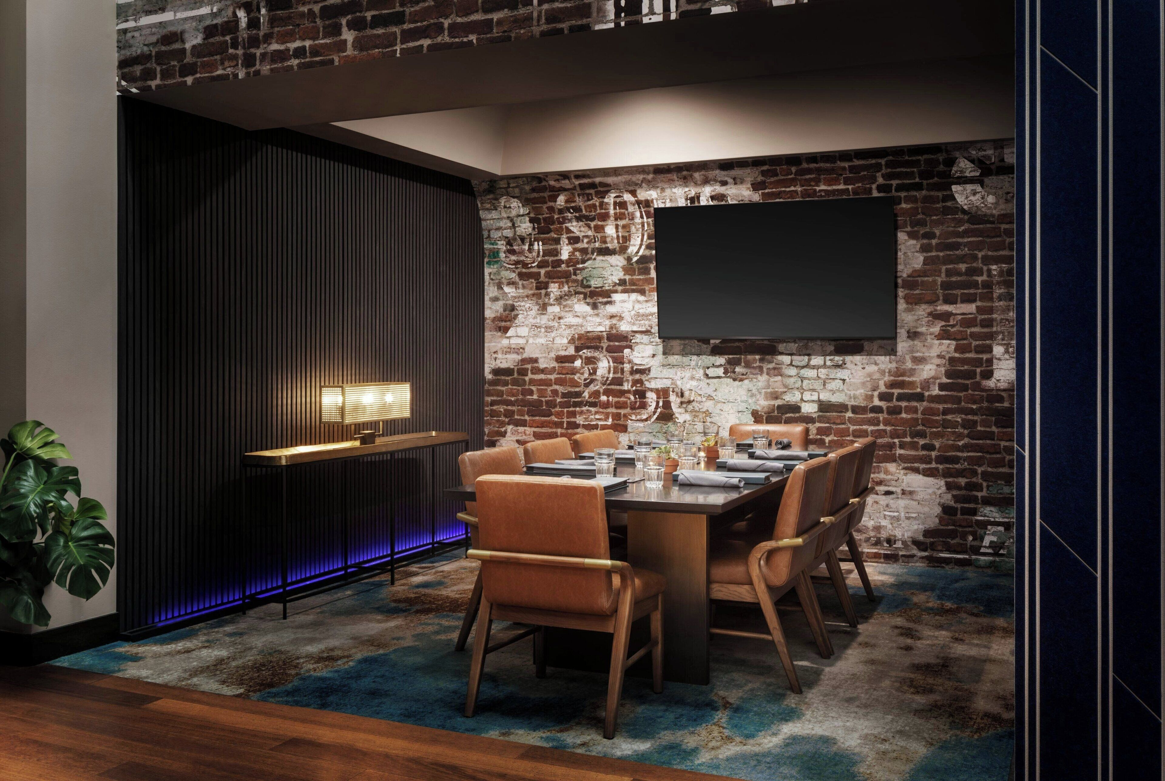 A dining area with a brick wall, a flat-screen TV, a modern bar area, and a large potted plant.