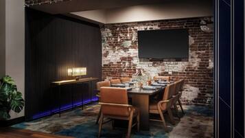 A dining area with a brick wall, a flat-screen TV, a modern bar area, and a large potted plant.