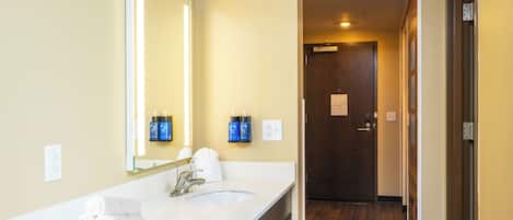 A hotel bathroom with a white sink, a large mirror, and two toiletries dispensers.