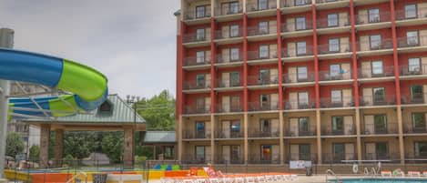 A hotel with a swimming pool, a water slide, and a multi-story building with balconies.