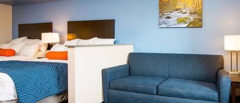 A hotel room with a bed, a blue sofa, a painting of a river, and a patterned carpet.