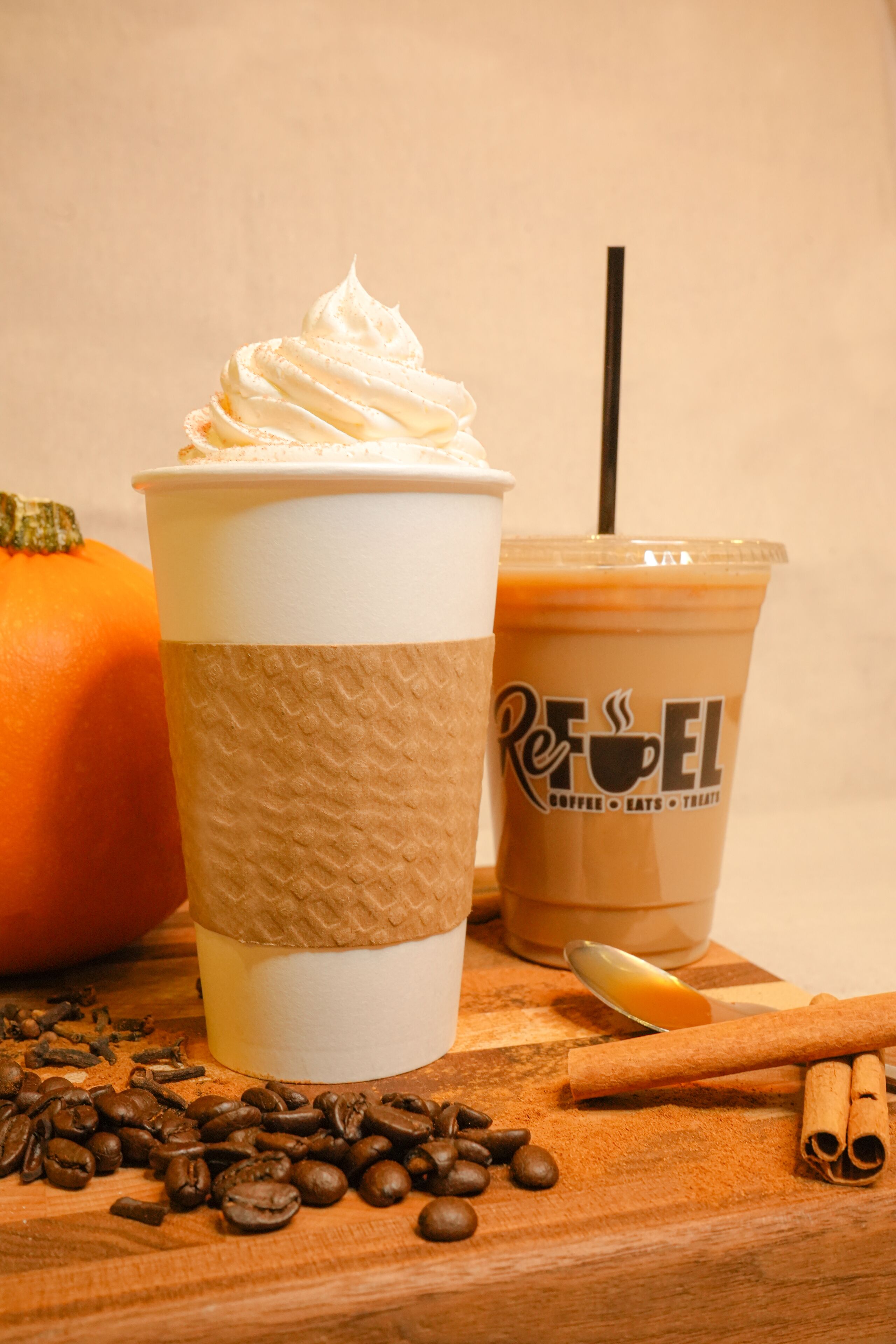 A cup of iced coffee with whipped cream and a straw, a pumpkin, and scattered coffee beans on a wooden surface.
