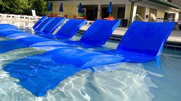 A swimming pool with blue lounge chairs and a building in the background.
