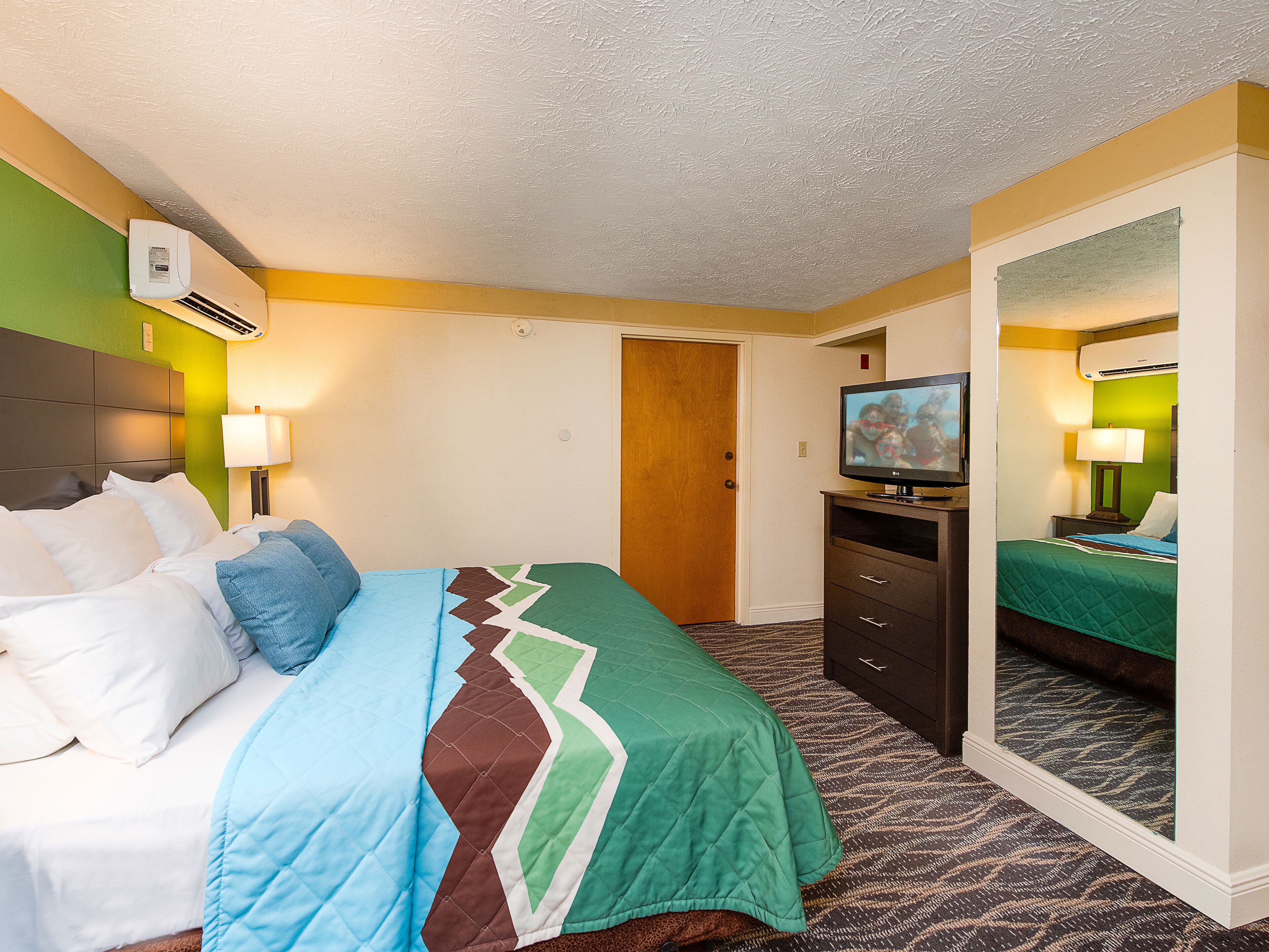 A hotel room with a bed, a TV, a dresser, and a mirror.