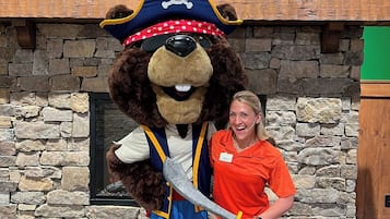 A mascot in a bear costume with a pirate hat and a sword, standing in front of a stone wall with a painting above.