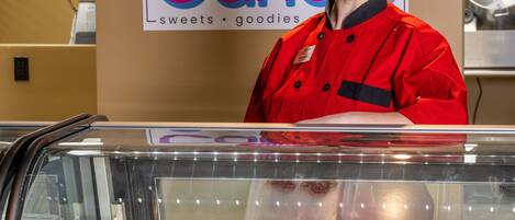 A bakery display case with various baked goods and a person in a red uniform behind it.