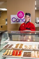 A bakery display case with various baked goods and a person in a red uniform behind it.