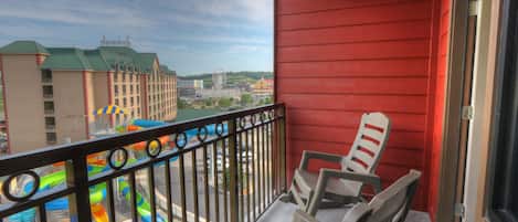 A balcony with a view of a water park, including a colorful water slide and a Ferris wheel.
