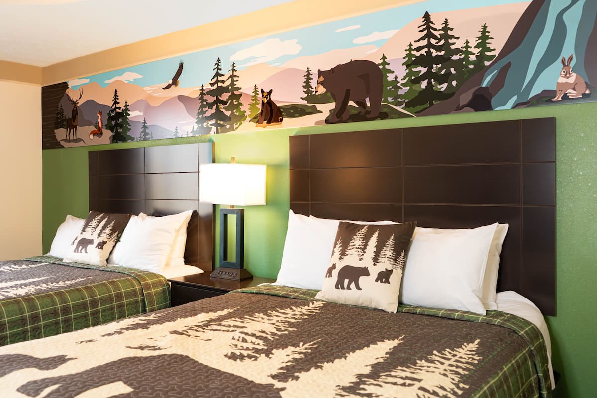 Une chambre d’hôtel avec deux lits, des murs verts et une fresque représentant des animaux de la forêt.