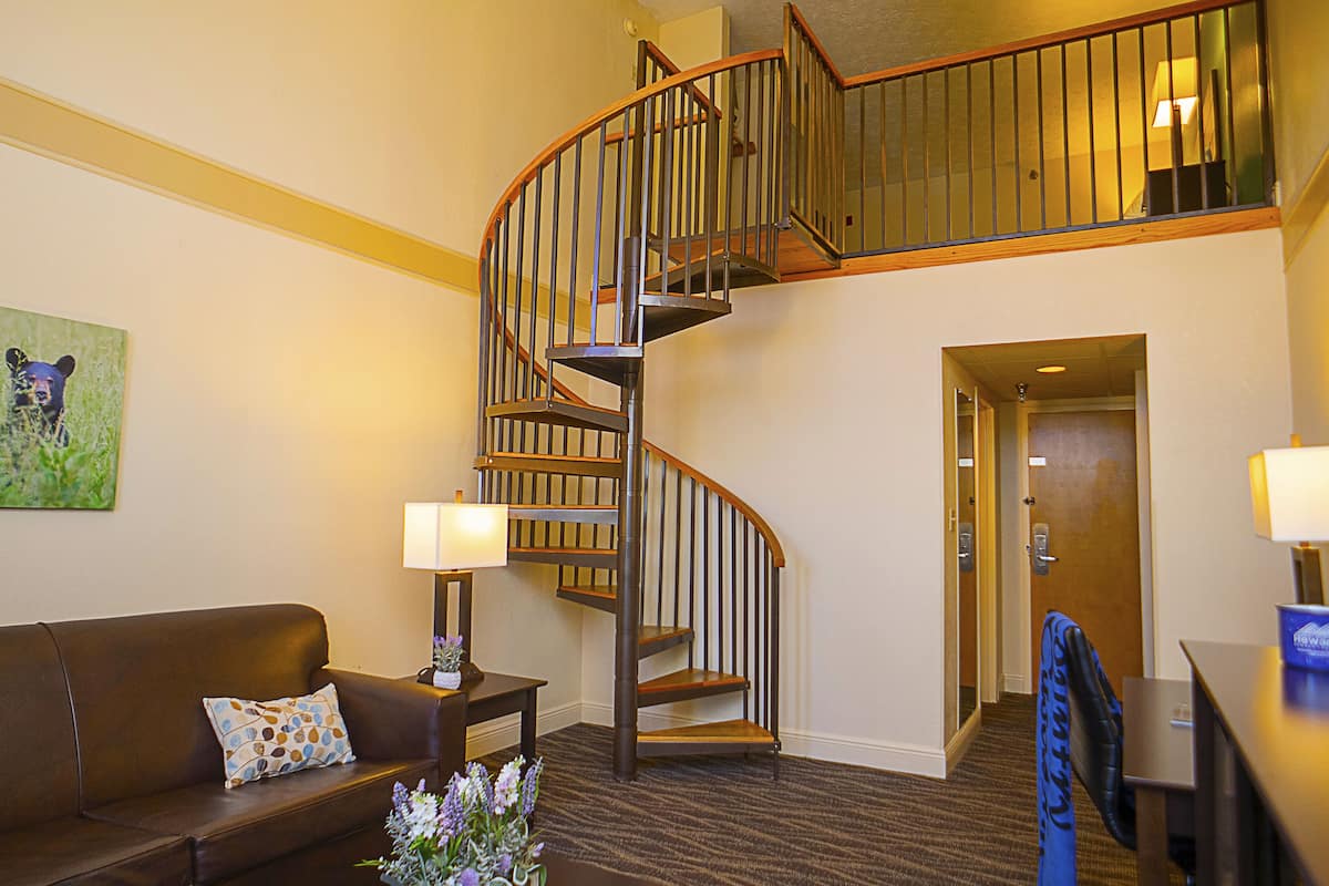 Un hall d’hôtel avec un canapé en cuir marron, un escalier en bois et une porte donnant sur une autre pièce.