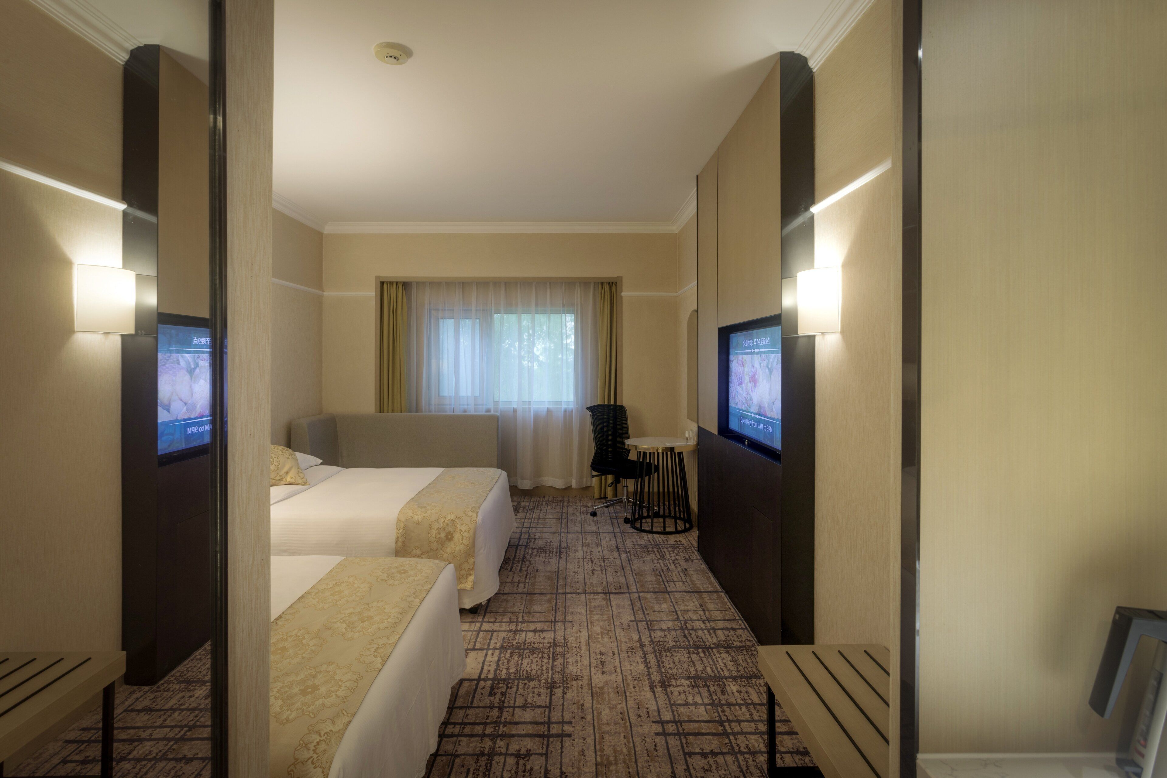 A hotel room with two beds, a desk, a chair, a TV, and a window with curtains.