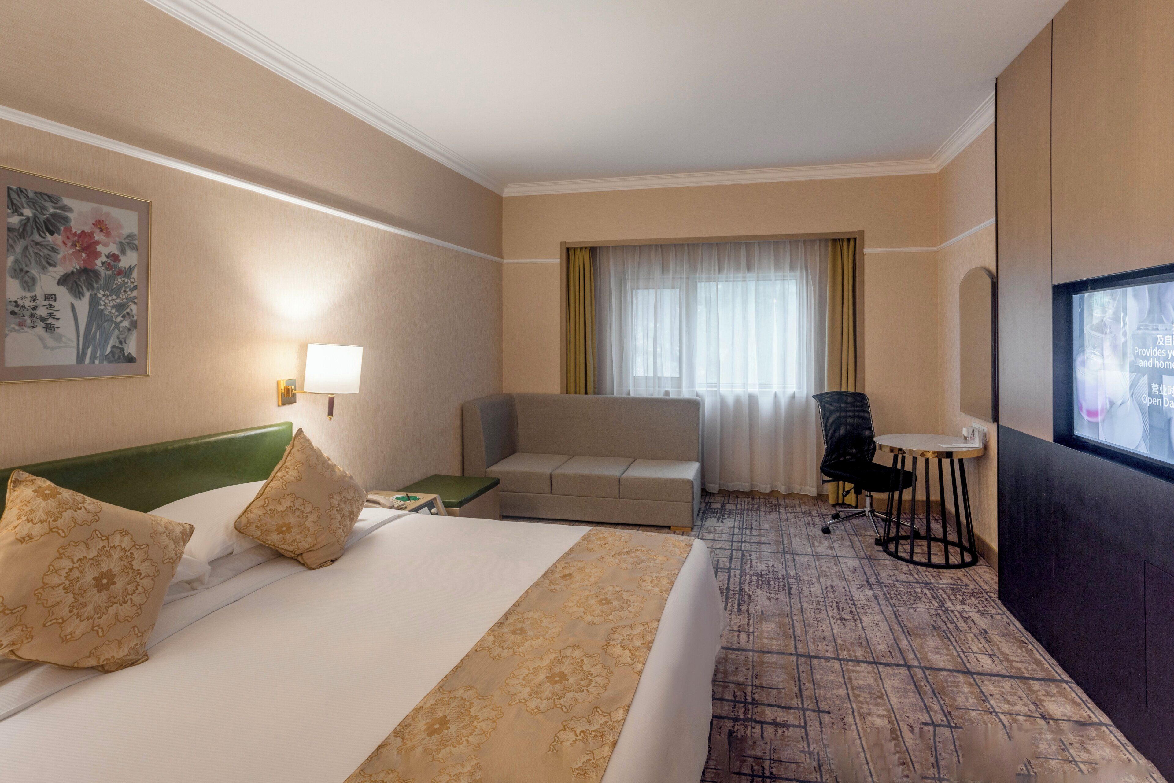 Hotellihuone, jossa on sänky, sohva, työpöytä, tuoli, ikkuna verhoilla ja taulu seinällä.
