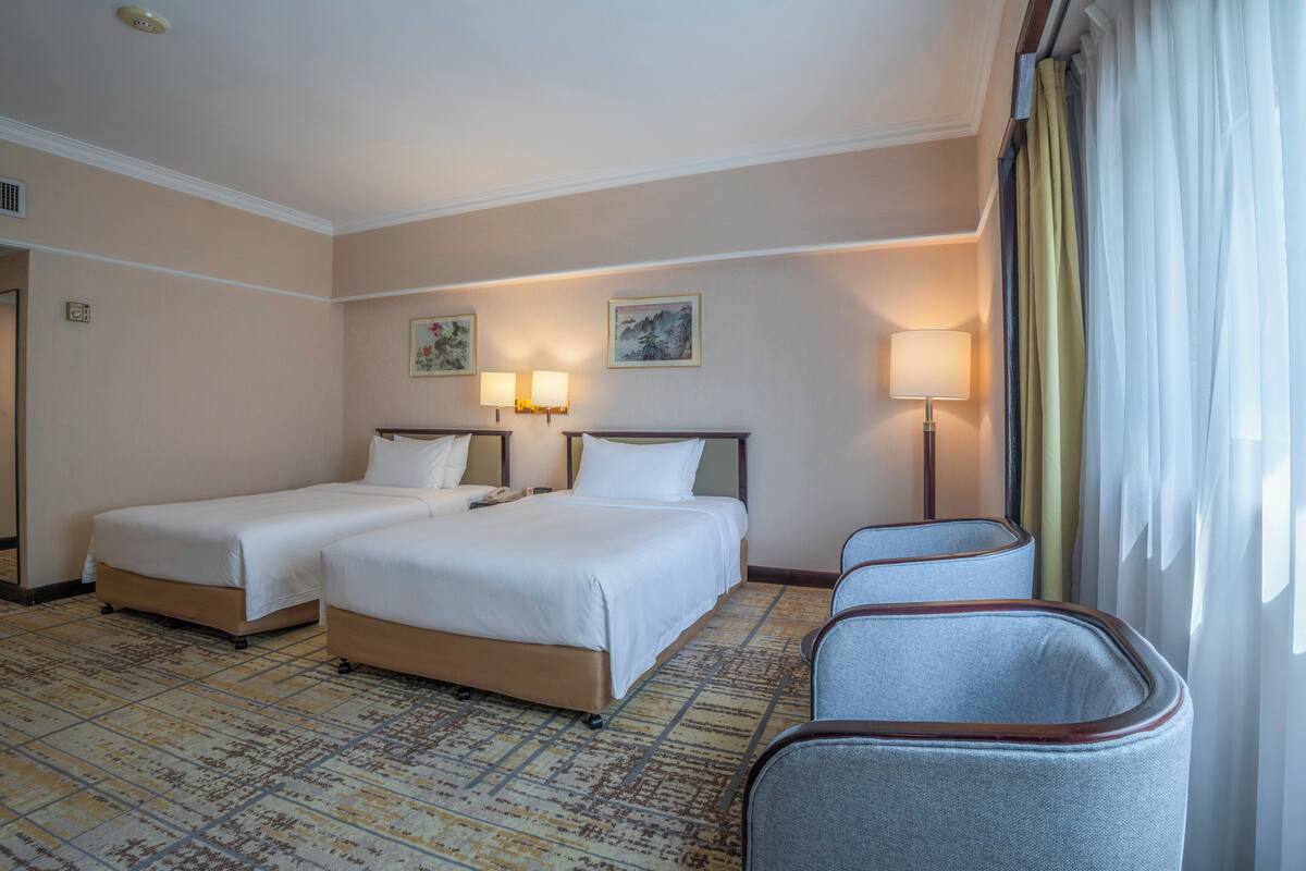 A hotel room with two beds, a sitting area with chairs, and a large window with curtains.