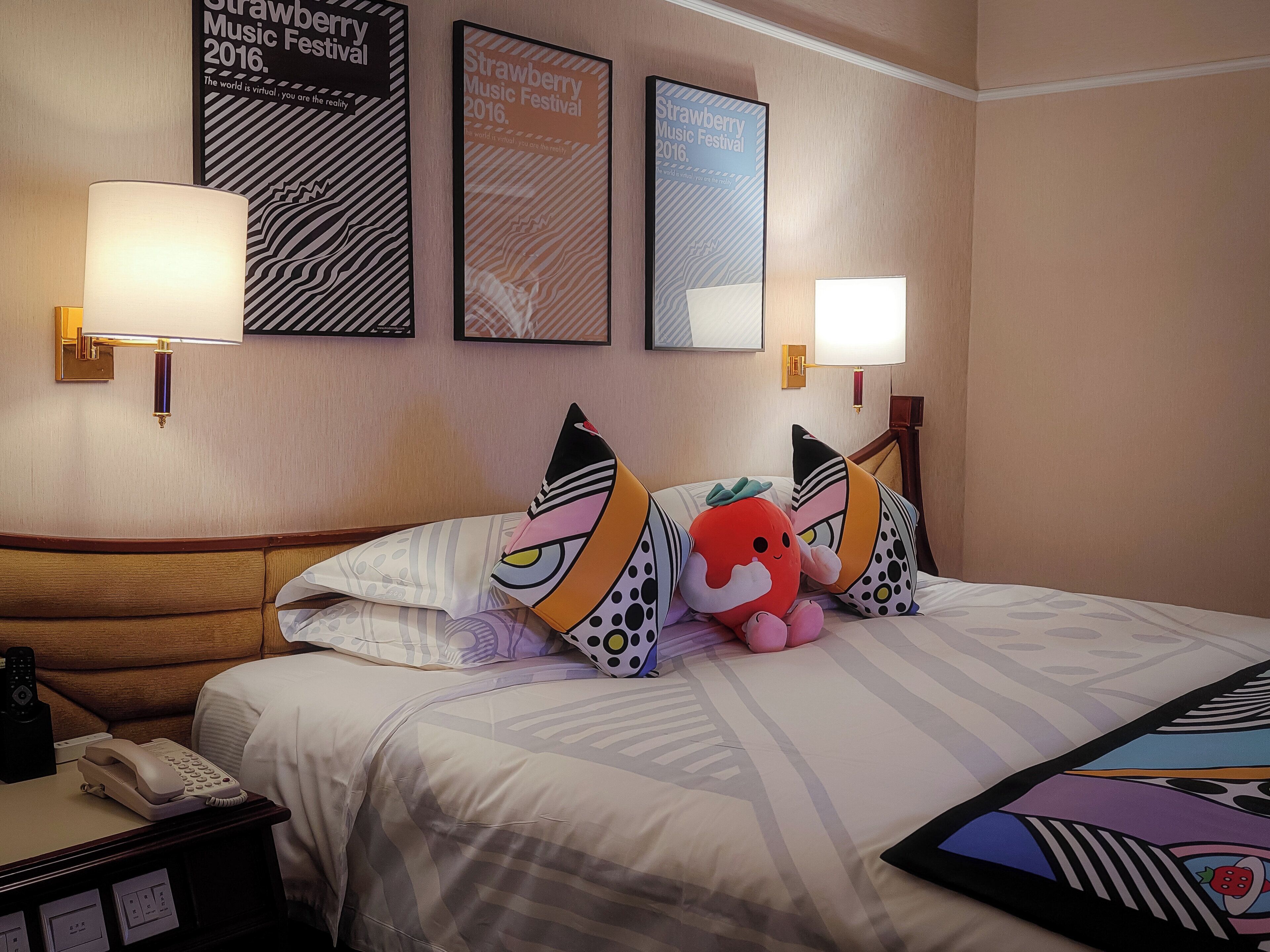 A hotel room with a bed, pillows, a lamp, a phone, and framed posters on the wall.