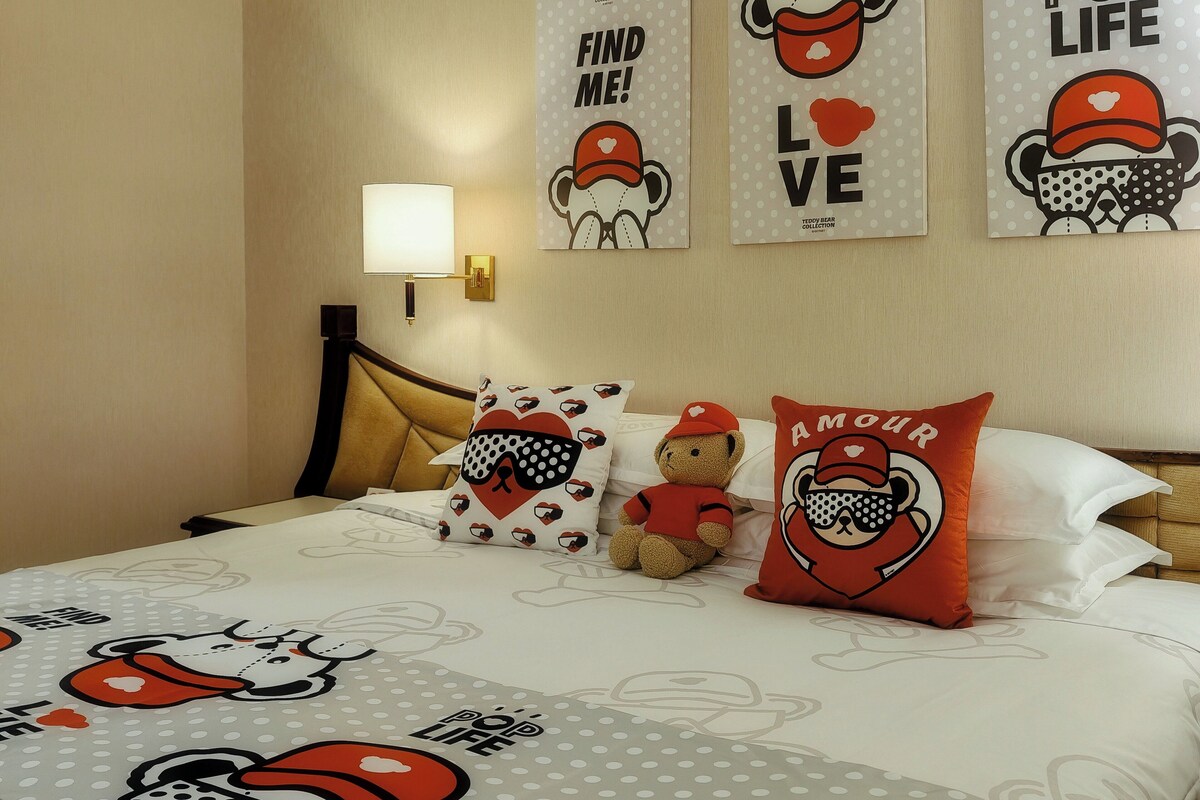 A hotel room with a bed, pillows, and wall art featuring a bear theme.