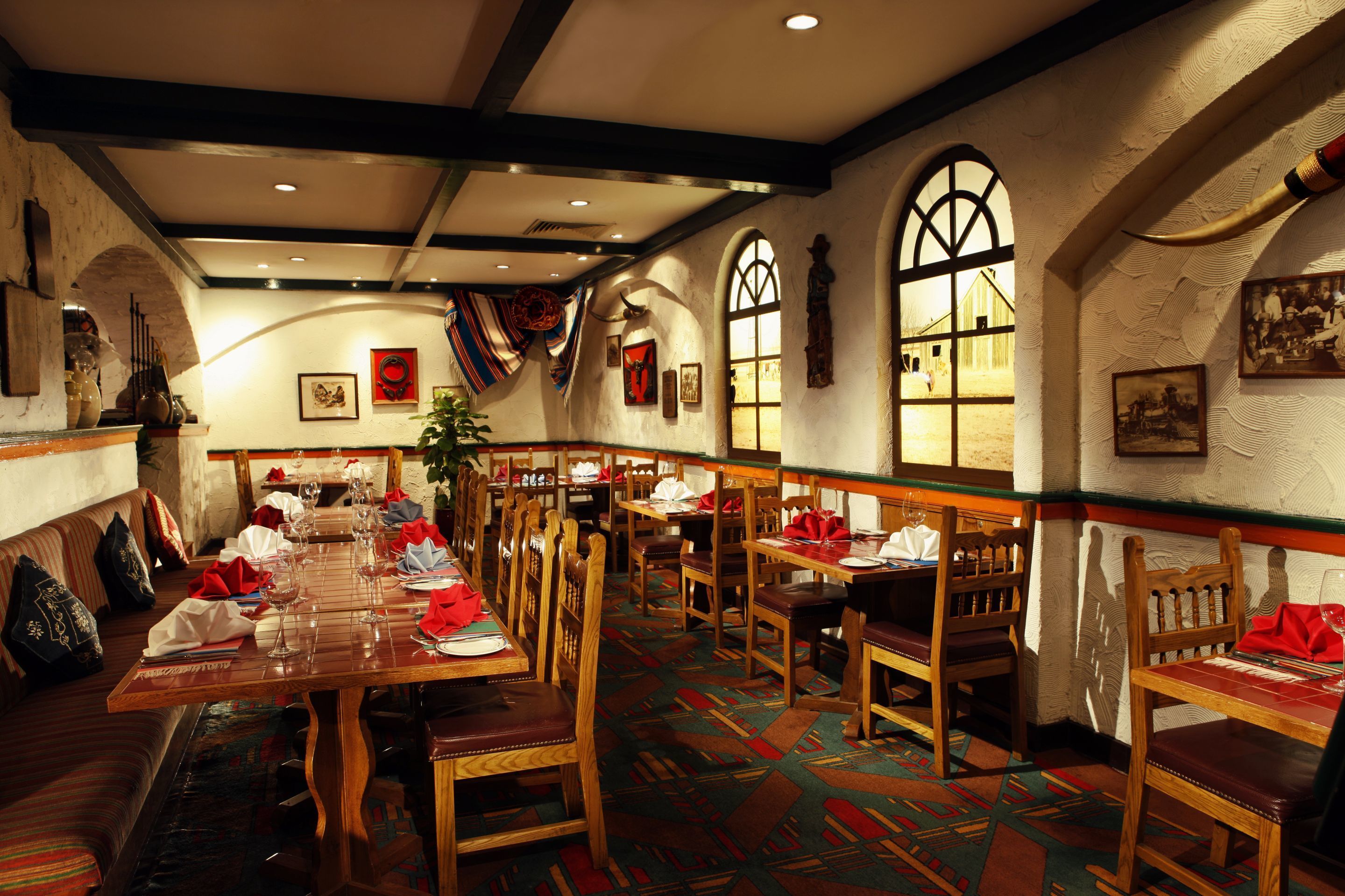 A restaurant with wooden tables and chairs, large windows, and a patterned floor.