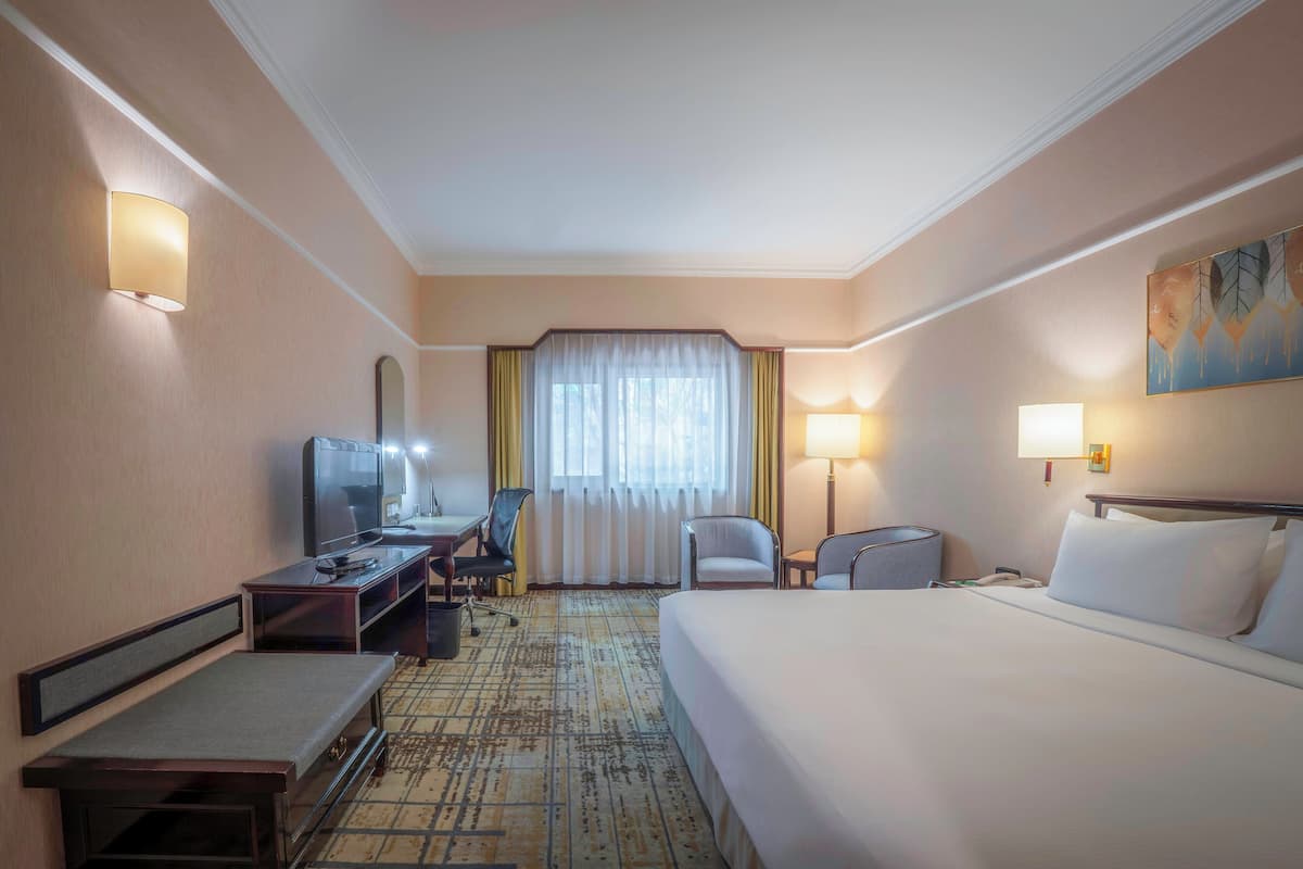 A hotel room with a bed, desk, chair, TV, and a window with curtains.
