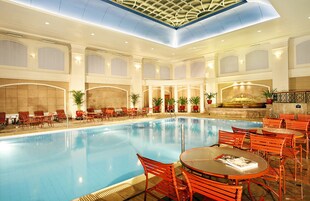 Ein großes Hallenbad mit roten Stühlen und Tischen, umgeben von Säulen und Kübelpflanzen.