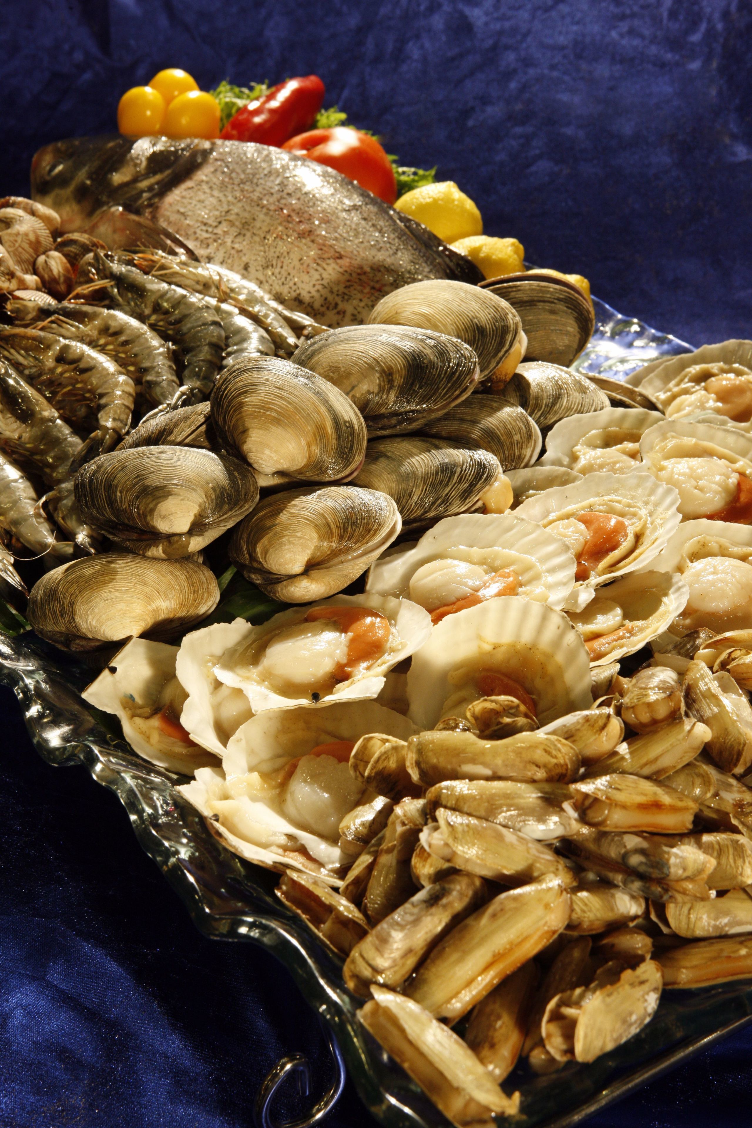 A seafood platter with clams, shrimp, and a fish on a glass dish.