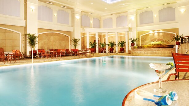 Ein Hallenbad mit roten Stühlen und Tischen, einer Fontäne und Topfpflanzen.