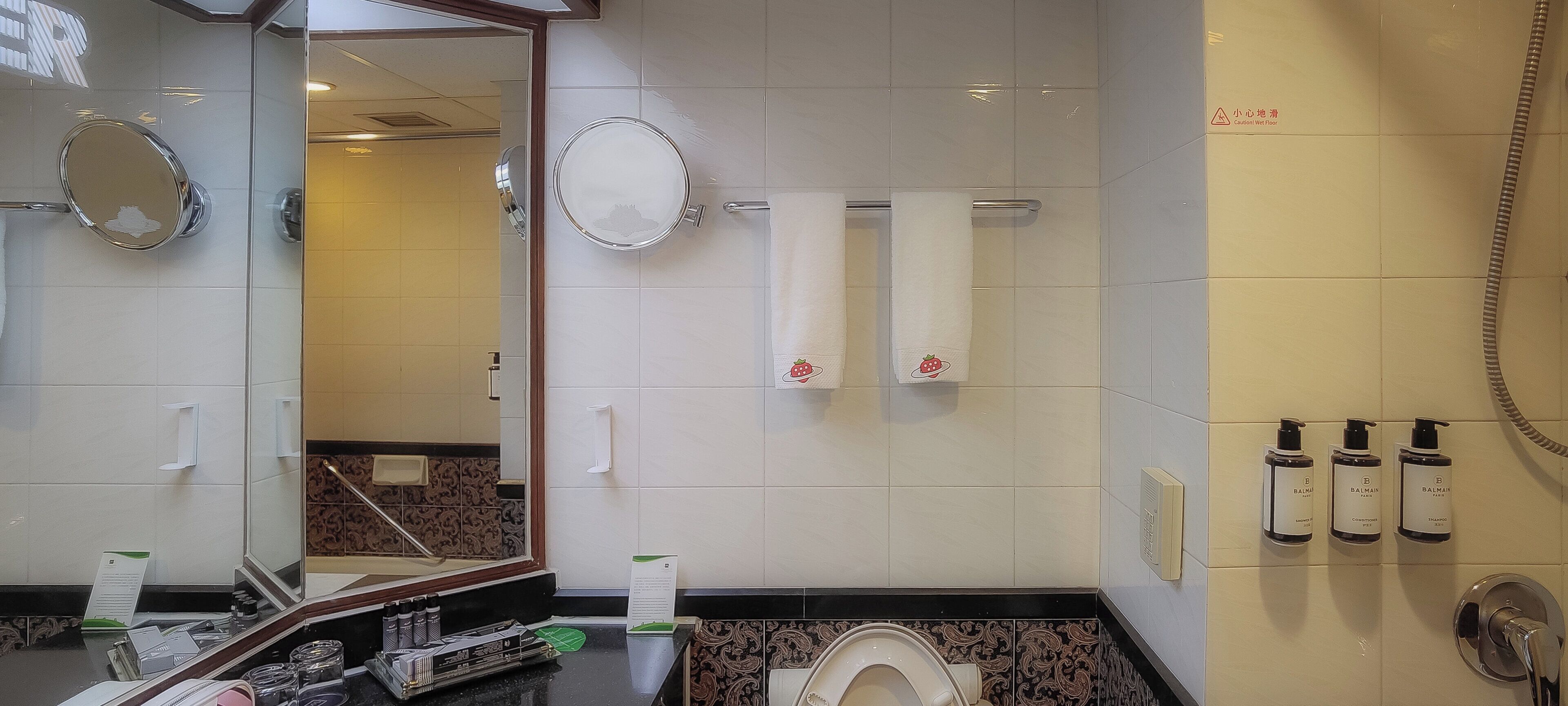 Un baño con inodoro, dos espejos, ducha y tres botellas de champú.