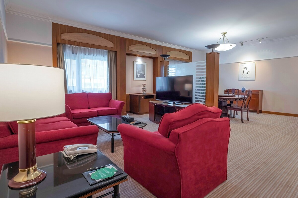 A hotel room with a red sofa, a TV, a lamp, and a dining area.
