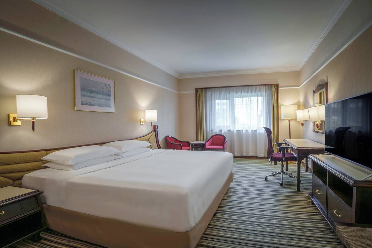 A hotel room with a large bed, a desk, a chair, a TV, and a window with curtains.