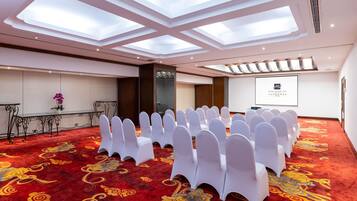 Una sala de conferencias con sillas blancas, alfombra roja y una pantalla para presentaciones.