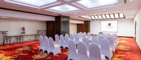 A conference room with white chairs, a red carpet, and a presentation screen.