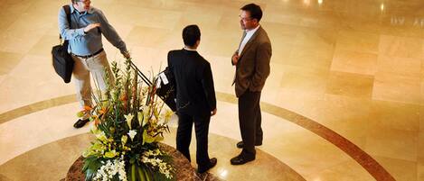 A lobby with a marble floor, a central floral arrangement, and three individuals in business attire.