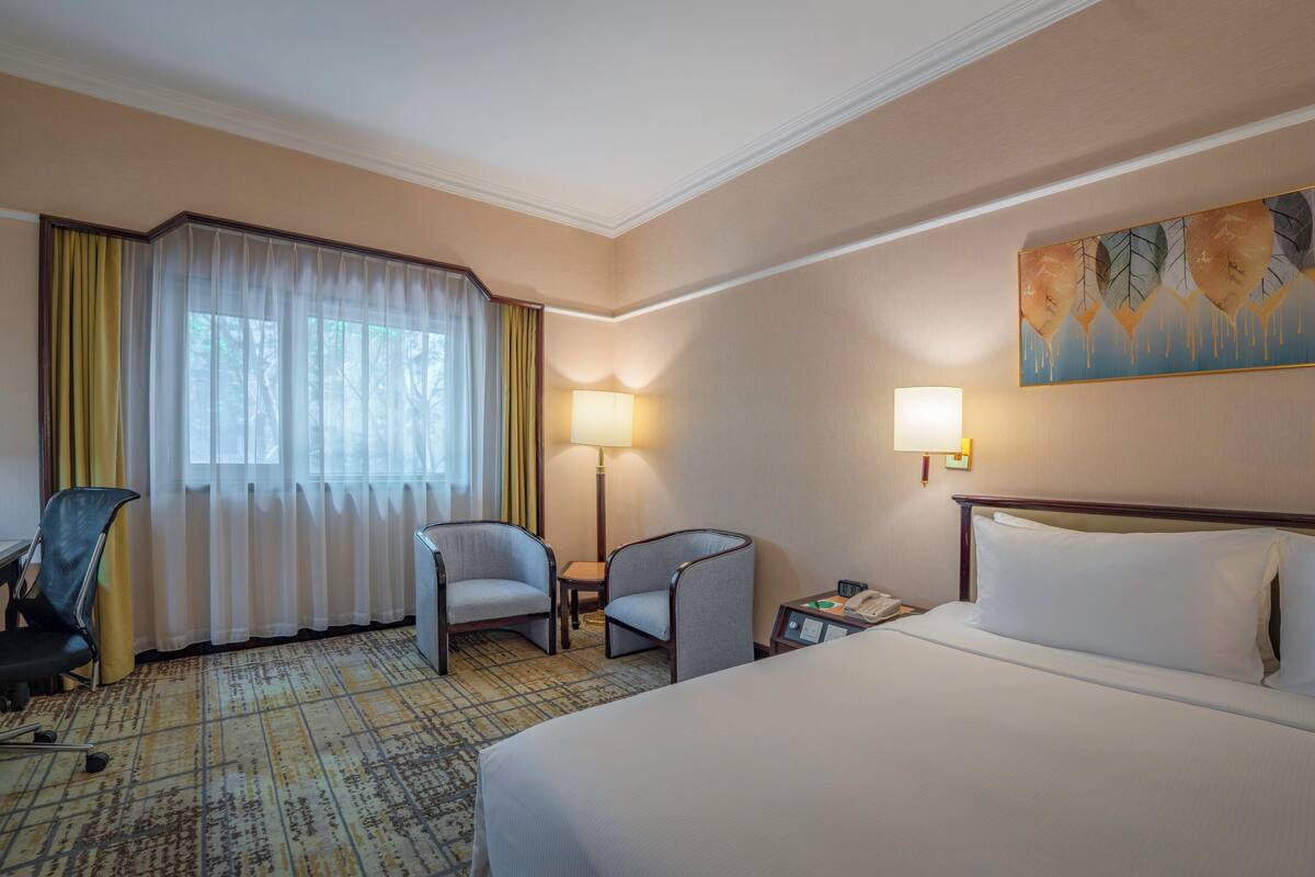 A hotel room with a large bed, two armchairs, a desk, a lamp, and a painting on the wall.