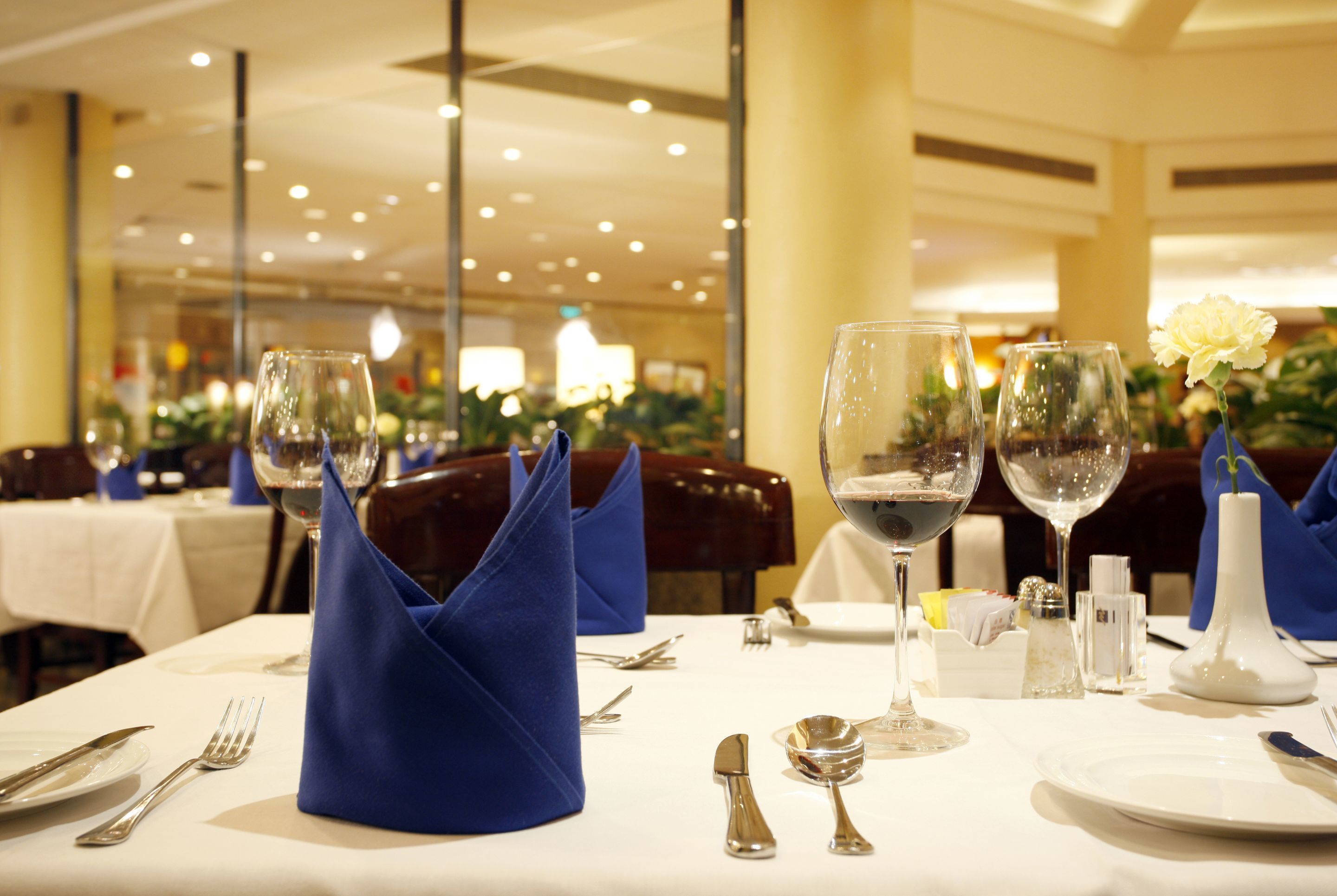 Une table à manger dressée avec des serviettes bleues, des verres à vin et des couverts en argent.