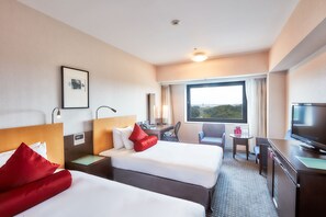 A hotel room with two beds, a desk, a chair, a TV, and a window with a view.