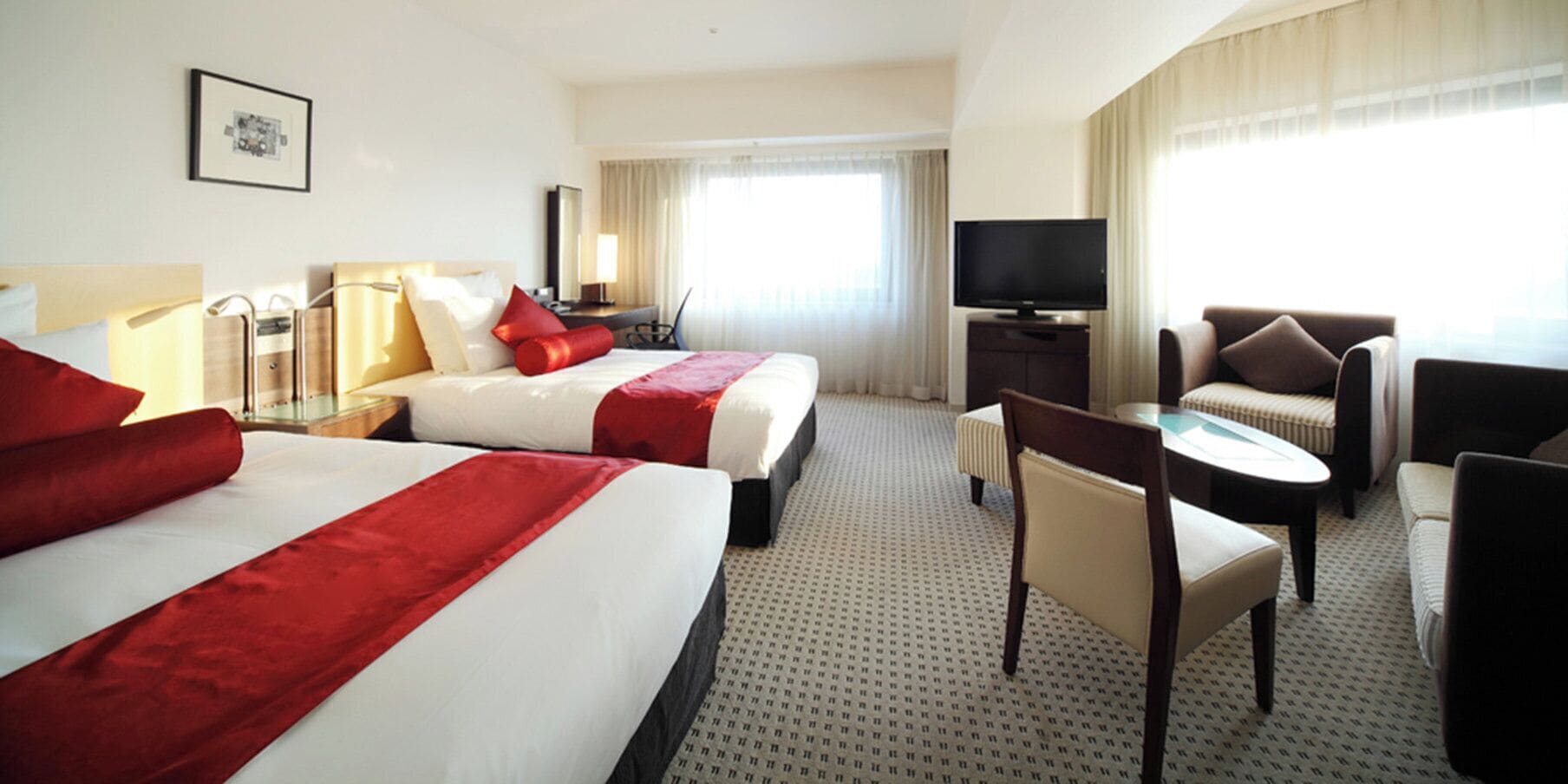 Una habitación de hotel con dos camas, televisión, escritorio y una silla.