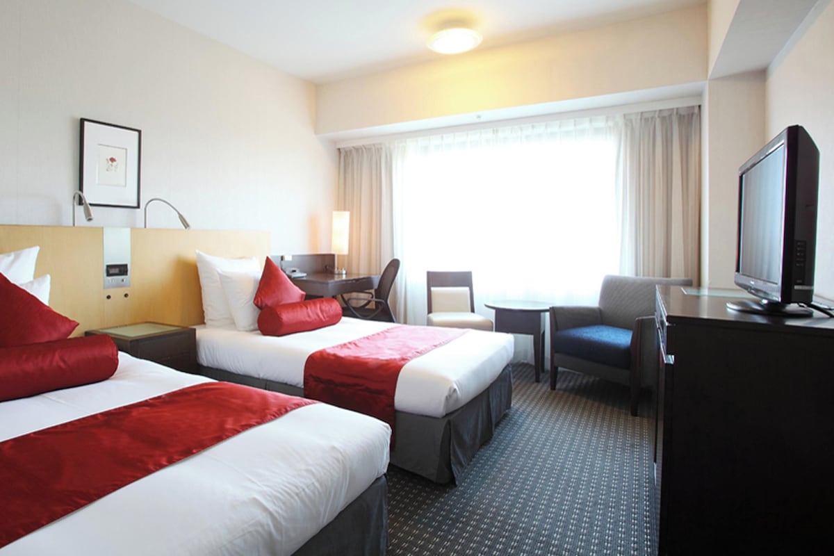 Hotelkamer met twee bedden, een bureau, een stoel, een televisie en een raam met gordijnen.