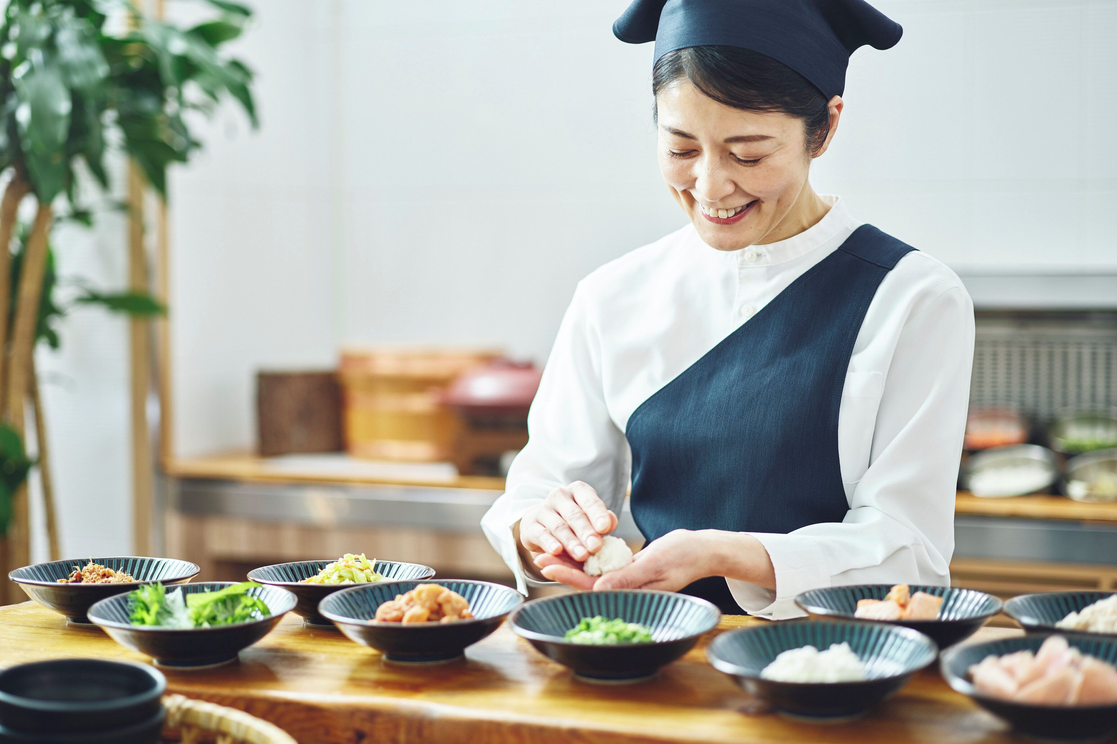 A person serving food in a restaurant setting with multiple bowls of dishes on a wooden table.